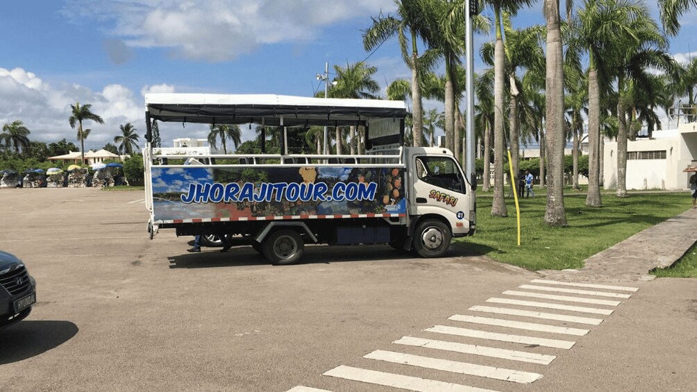 A safari truck parked on a street with palm trees and a crosswalk. 2