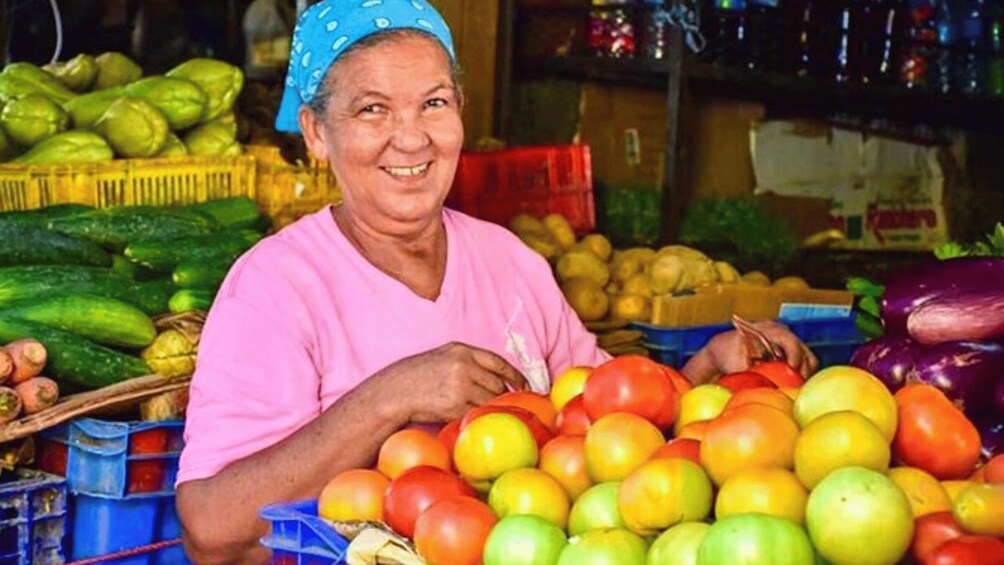 A person at a fruit market with various fruits like apples and tomatoes. 3