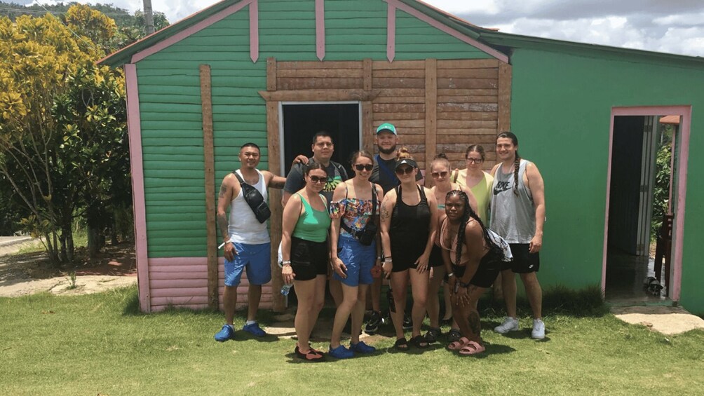 A group of people standing in front of a green wooden shed with a pink trim. 5