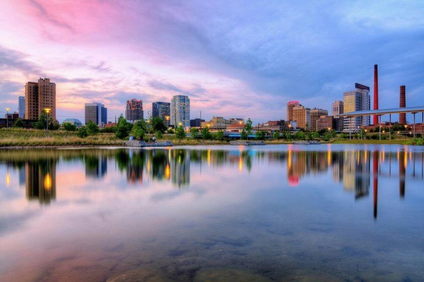 A city skyline at dusk with buildings reflected in a calm body of water. 2