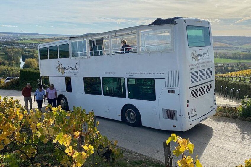 Un autobus à deux étages, sur lequel on peut lire le mot « Impérial », est garé sur une route, avec un vignoble en arrière-plan. 1