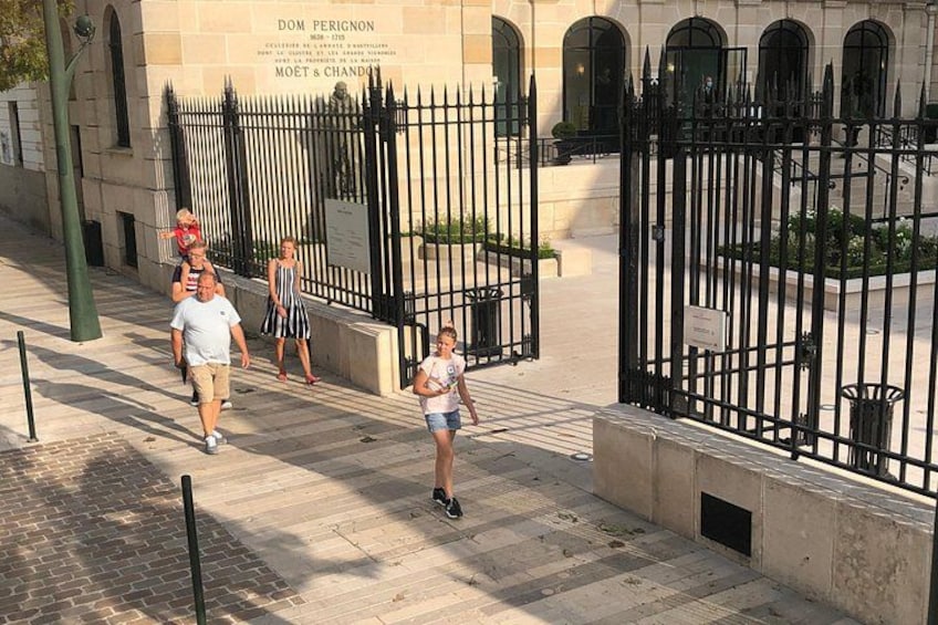 A group of people walking on a paved path beside a black metal fence with a building in the background. 4