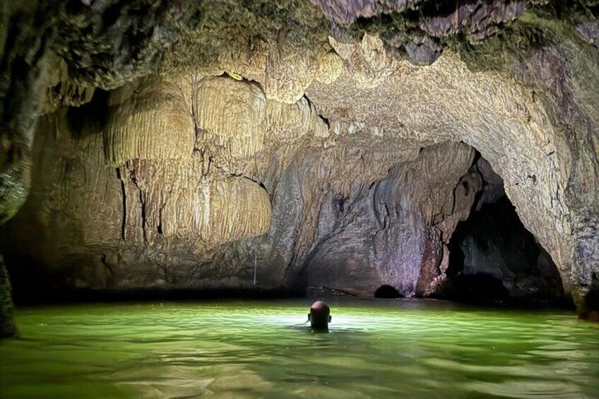 A cave with stalactites and stalagmites, water, and a person swimming. 1