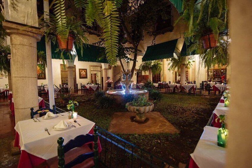 An outdoor dining area with tables and chairs, a fountain, and tropical plants. 3