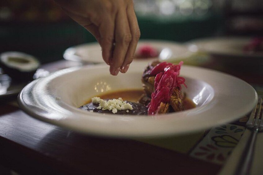 A hand sprinkling a red condiment on a dish. 2