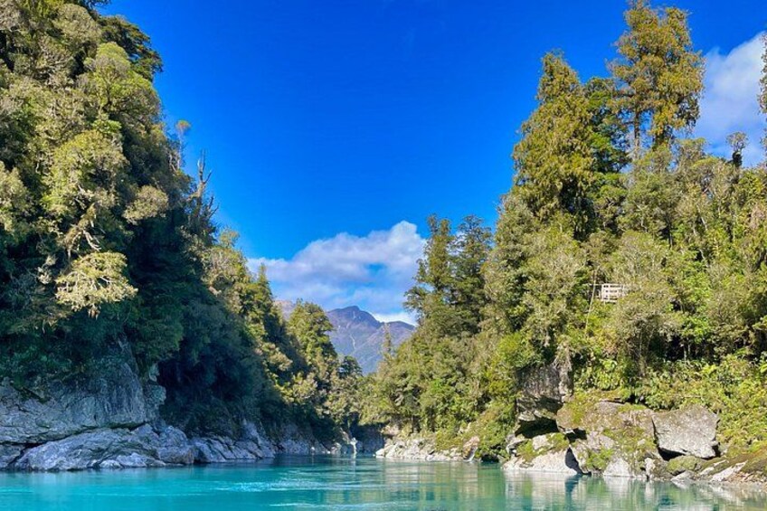 A river surrounded by dense forest and rocky cliffs under a clear blue sky. 1