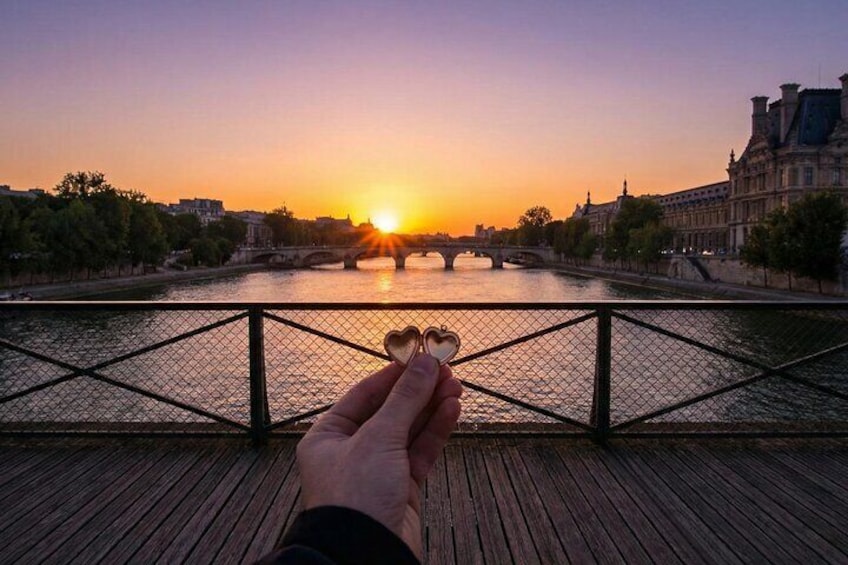A sunset over a river with a bridge, a hand holding a heart-shaped object, and a wooden deck. 4