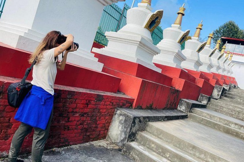 Eine Person fotografiert eine Reihe weißer und roter Stupas mit goldenen Spitzen. 3