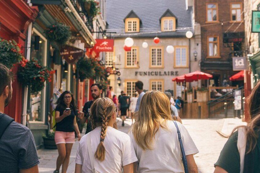 A street with people walking, a building with a sign that reads 'FUNICULAIRE,' and hanging plants. 2