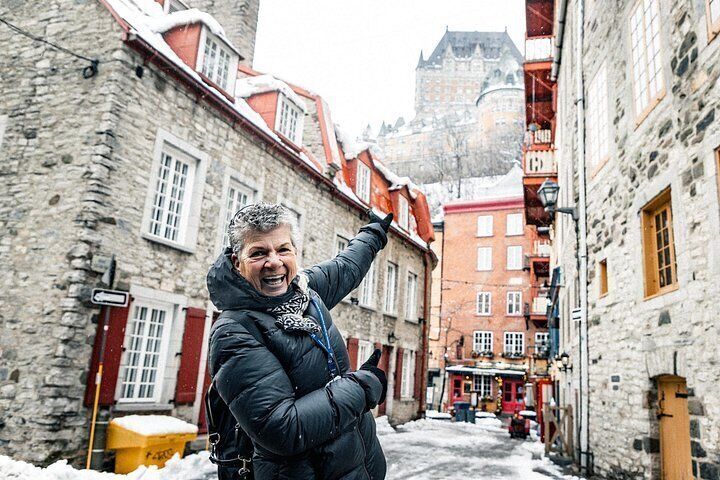 A person in a black jacket standing in a narrow street with stone buildings and a castle in the background. 5