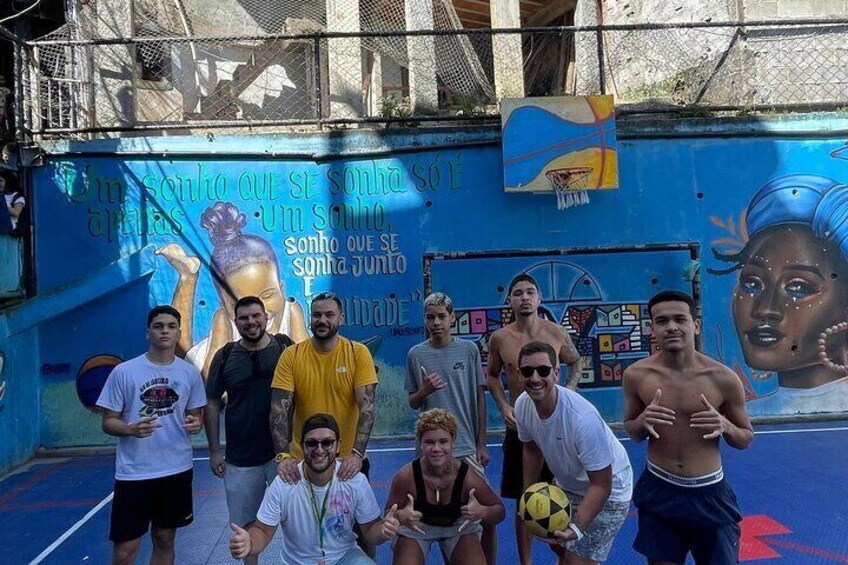 Un groupe de personnes posant devant une fresque murale colorée, avec un terrain de basket en arrière-plan. 3