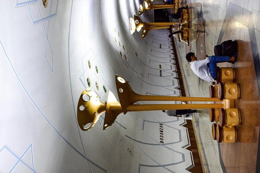 A modern interior with a large golden sculpture, seating areas, and a person with luggage. 5