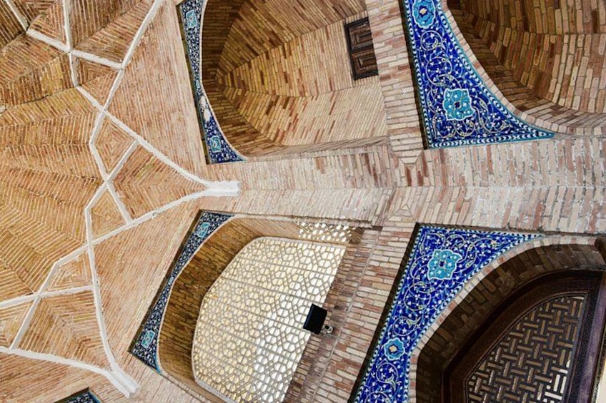Dettaglio di un pavimento piastrellato con motivi geometrici e una porta in legno con decorazioni elaborate. 5