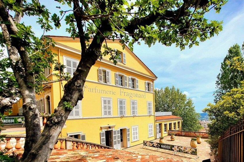 Un edificio giallo con il cartello 'Parfumerie Fragonard' e un cortile con piastrelle. 1