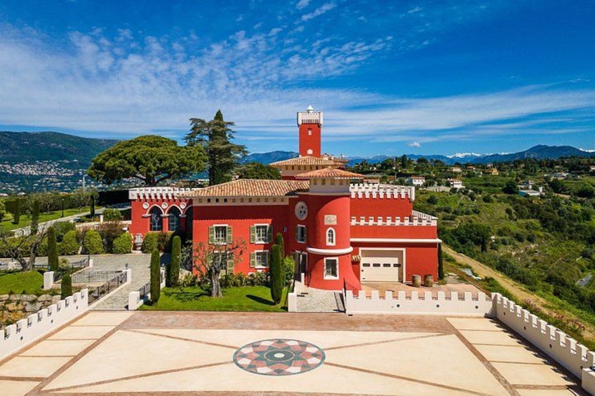Un edificio rosso con una torre, circondato da un giardino curato e un pavimento decorato. 2