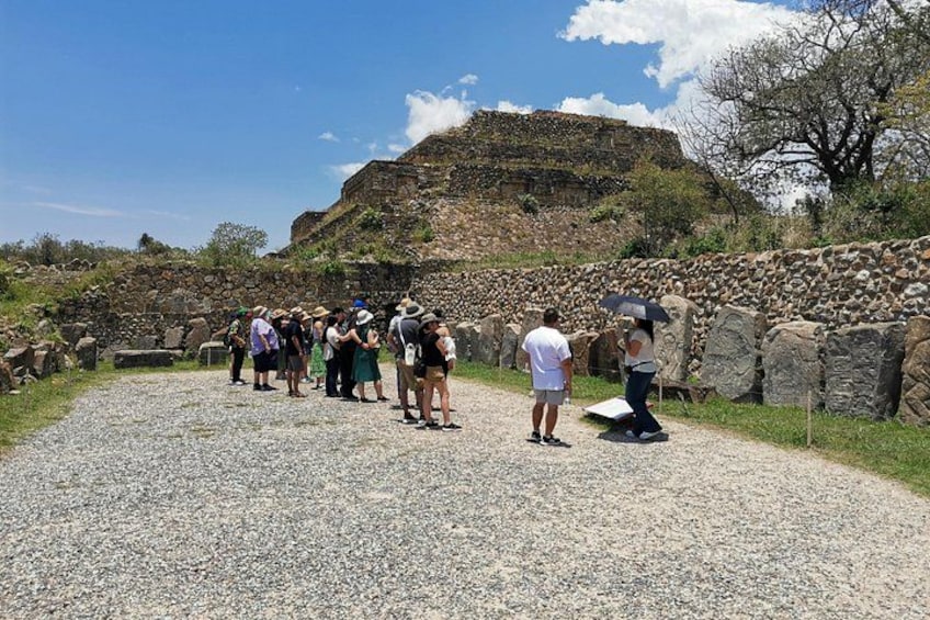A group of people standing on a gravel path, observing a historical site with stone walls and a hill in the background. 3