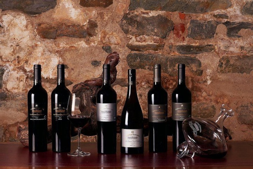 Une collection de bouteilles de vin et un verre posés sur une surface en bois, avec un mur de pierre en arrière-plan. 2