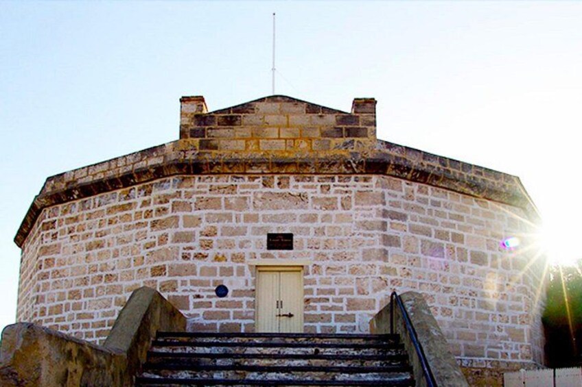 A stone building with a round shape, a door, and a staircase leading up to it. 2