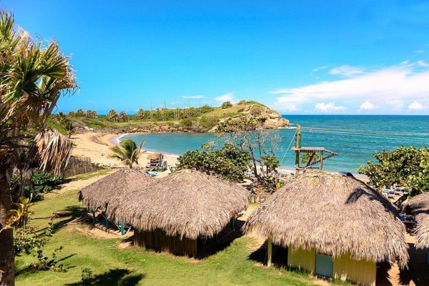 A beach with thatched-roof huts, a clear blue sky, and a calm sea. 3