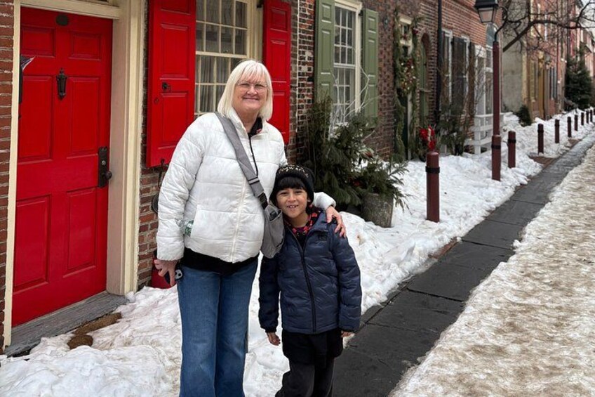 A person standing in front of a red door, another person with a backpack, and a snow-covered sidewalk. 3