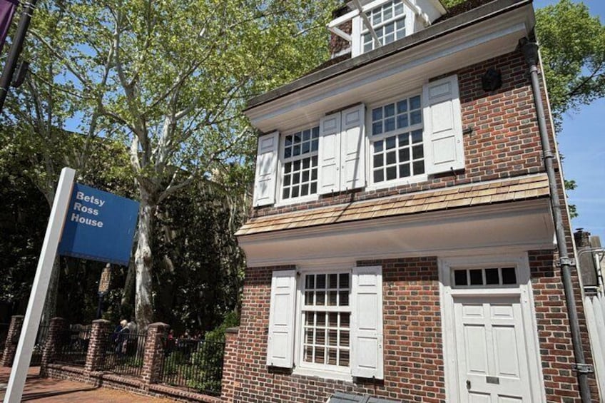 A two-story brick house with white shutters and a blue sign reading 'Betsy Ross House.' 2