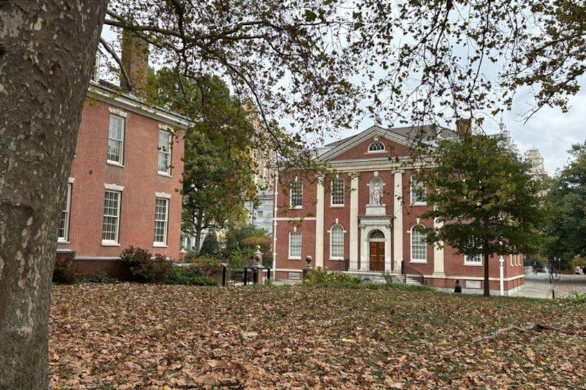 A red brick building with a central entrance, surrounded by trees and fallen leaves. 5