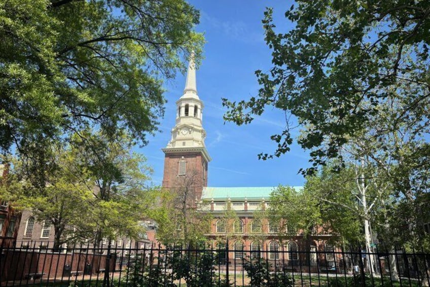 A church with a tall steeple, surrounded by trees and a fence. 3