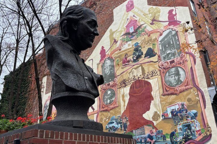 A statue of a woman with a mural in the background. 1