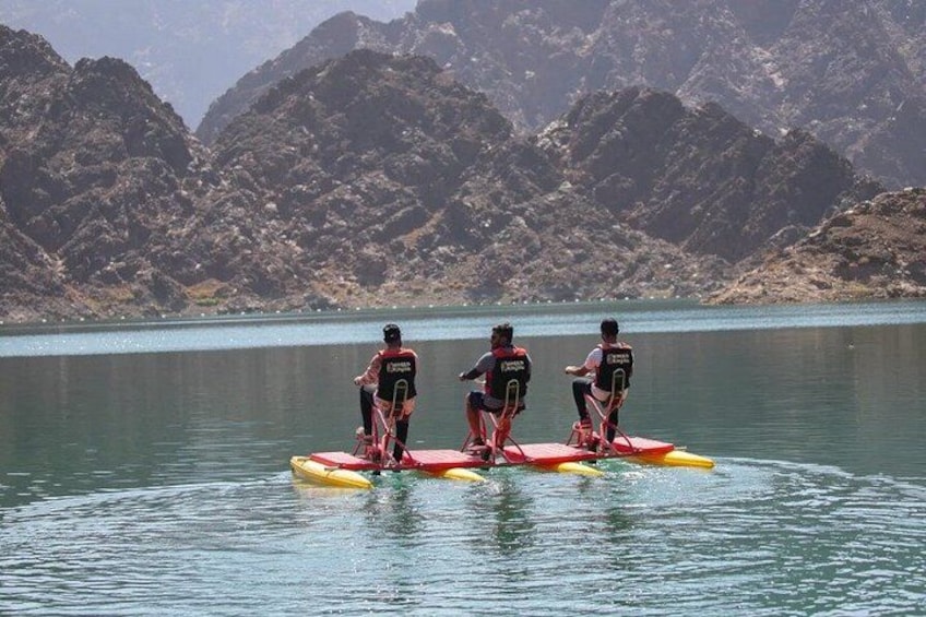 Tres personas en una balsa roja en un lago tranquilo, con montañas al fondo. 2