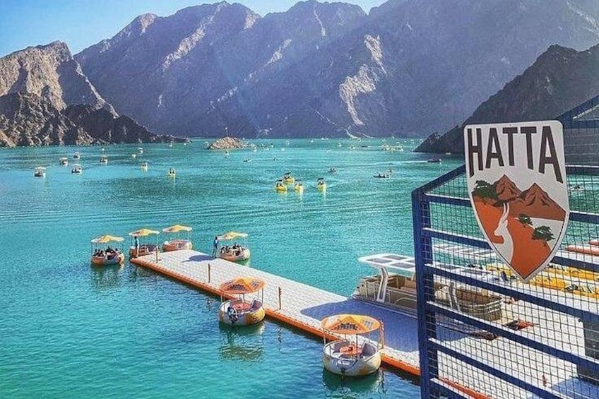 Una zona costera con barcos, un muelle y montañas al fondo. 1