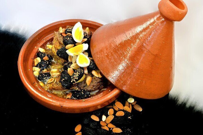 A tagine with a clay pot, containing a stew with almonds, raisins, and lemon slices. 4