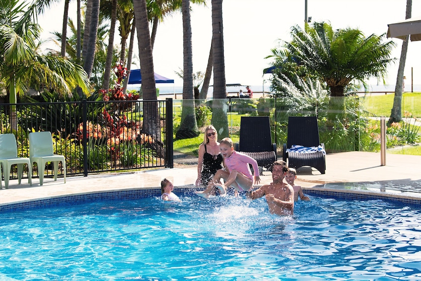A swimming pool with people enjoying the water, surrounded by palm trees and lounge chairs. 4