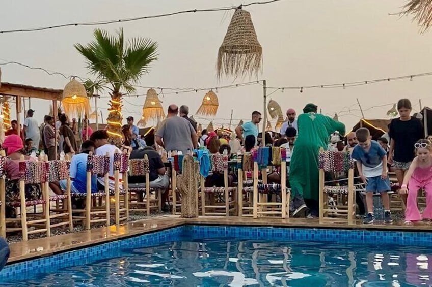 Un événement en plein air très fréquenté, avec une piscine, des personnes assises sur des chaises et des guirlandes lumineuses. 1