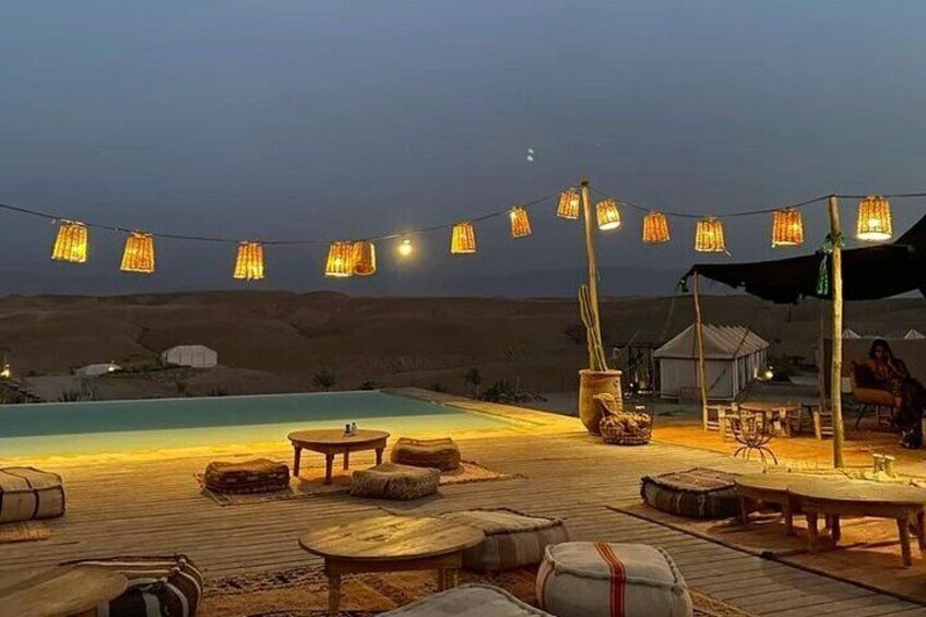 Un espace aménagé au bord de la piscine, agrémenté de guirlandes lumineuses, de mobilier en bois et offrant en arrière-plan un paysage désertique. 5