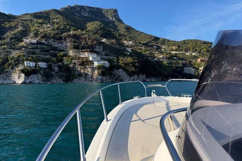 Ein Boot auf ruhigem Wasser mit einer gebirgigen Küstenlinie im Hintergrund. 2