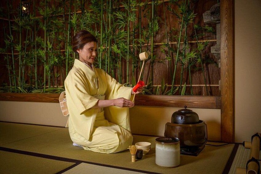 A person in traditional attire performing a tea ceremony with a tea set and a bamboo backdrop. 4