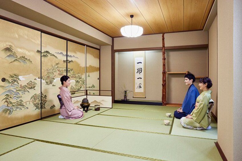 A traditional Japanese room with tatami flooring, sliding doors with artwork, and a hanging scroll with calligraphy. 1