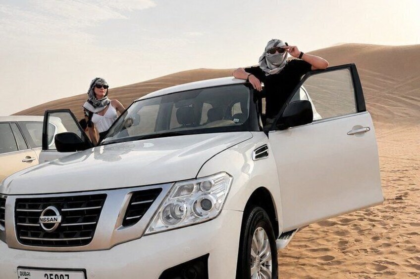 A white SUV parked in a desert with sand dunes in the background. 2