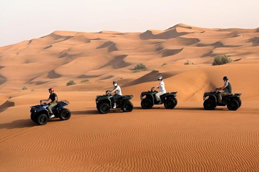 Three people riding quad bikes across a desert with sand dunes in the background. 4