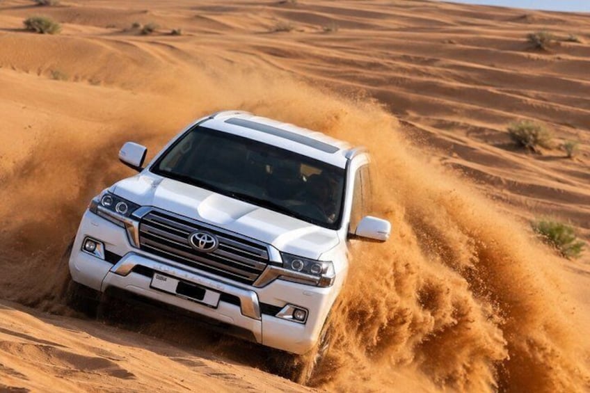 Ein weißer SUV fährt durch eine Wüste, dabei wirbeln Sandwolken auf. 1