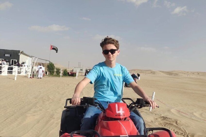 Eine Person fährt mit einem Quad über hügeliges Sandterrain, im Hintergrund weht eine Flagge. 5