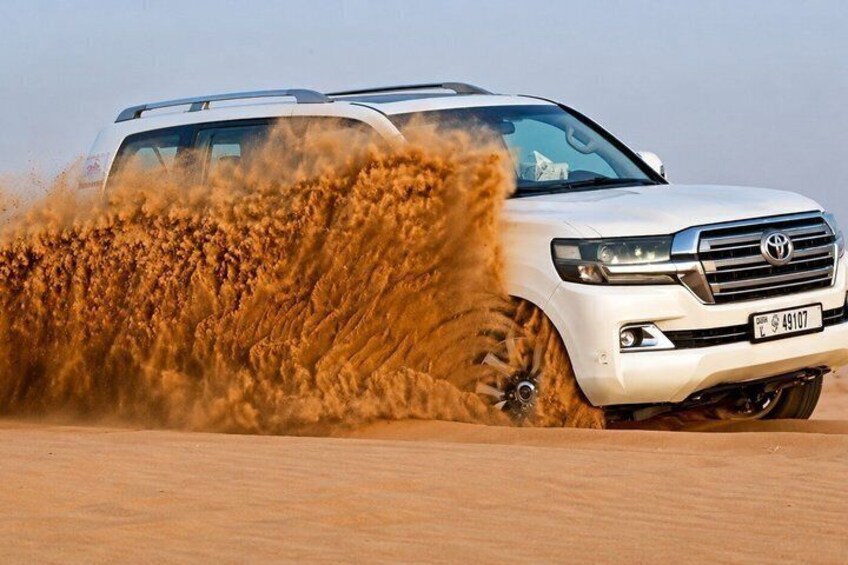 A white SUV driving through a sandy area, kicking up dust. 1