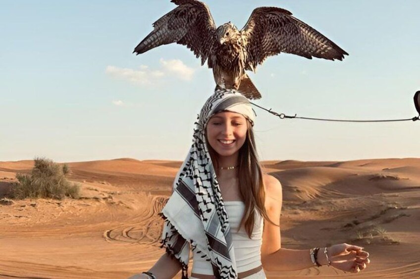 A person with a bird of prey on their head in a desert landscape. 5