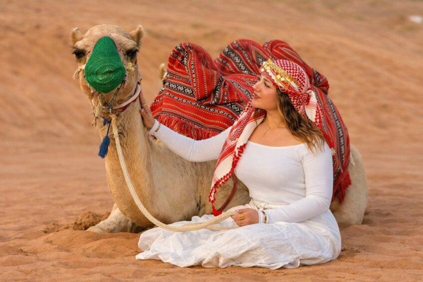 A person sitting on the sand with a camel. 2