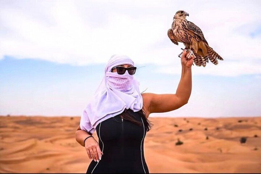 Eine Person hält in einer Wüstenlandschaft einen Greifvogel. 2