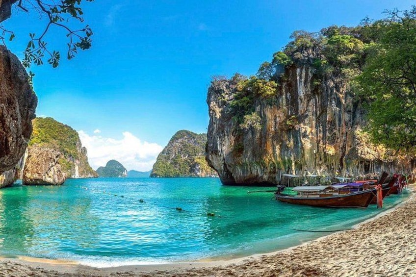 A beach with clear turquoise water, rocky cliffs, and a boat docked on the shore. 1