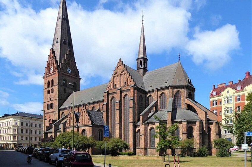 A large brick church with two prominent spires and a clock tower. 4