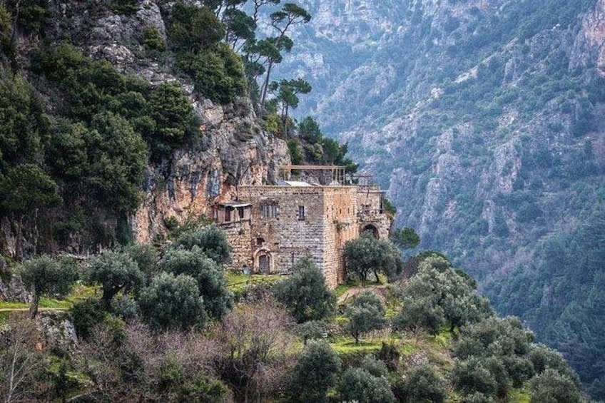A stone building perched on a mountain cliff surrounded by trees. 1