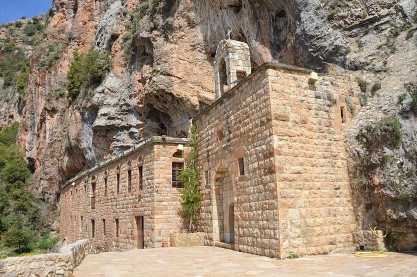 A stone building with a flat roof, set against a rocky cliff. 3
