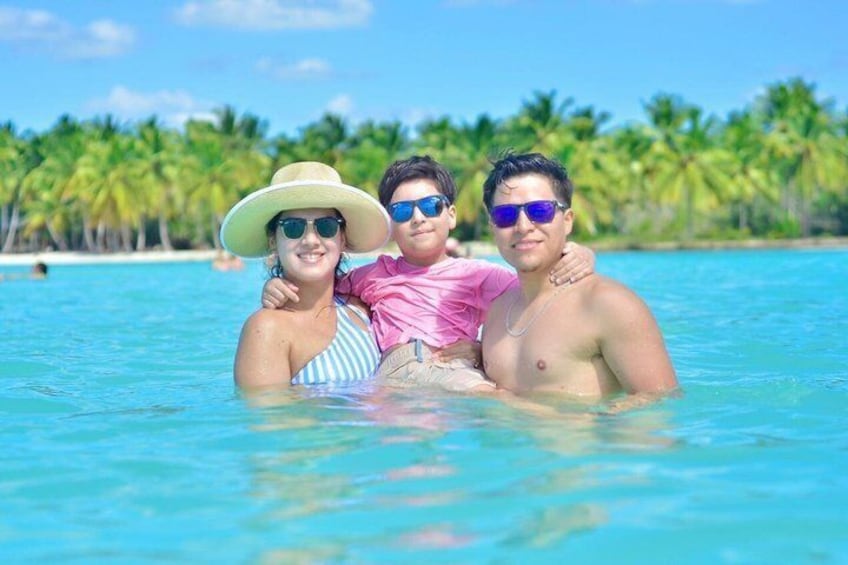 Un couple et un enfant dans une mer d’un bleu limpide, avec des palmiers en arrière-plan. 5